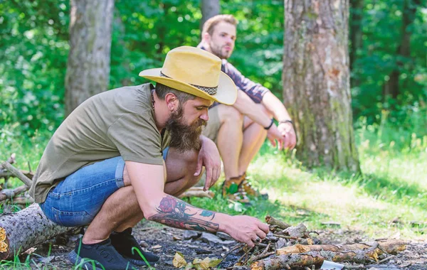 Homens de férias. Conceito de masculinidade. Guia final para fogueiras. Como fazer fogueira ao ar livre. Organizar os galhos da floresta ou paus de madeira. Homem brutal hipster barbudo prepara fogueira na floresta — Fotografia de Stock