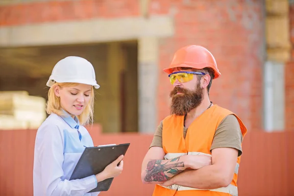 Construction project inspecting. Construction site safety inspection. Discuss progress project. Safety inspector concept. Woman inspector and bearded brutal builder discuss construction progress