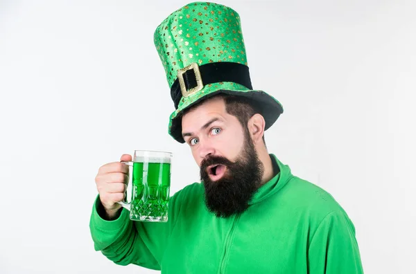 La elevación del verde. Hipster en sombrero de duende sosteniendo taza de cerveza. Celebrando el día de San Patricio en el bar. Un hombre barbudo brindando por el día de San Patricio. Irlandés con barba bebiendo cerveza verde — Foto de Stock