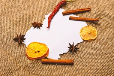Çul arka plan üzerinde kağıt parçası. Tarçın, kurutulmuş portakal ve biber, anasonu boş kağıt, tarifi, kopya alanı çevresinde. Baharatlar, beyaz kağıt mutfak otlar yatıyordu. Mutfak tarifi kavramı