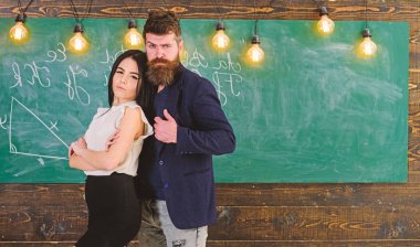 Öğretmen ve sıkı öğretmen rahat görünüyor. Bayan ve birlikte okulda çalışan hippi. Ortaklar kavramı. Sakal ve seksi kız öğretmen stand sınıfta, kara tahta arka plan ile adam