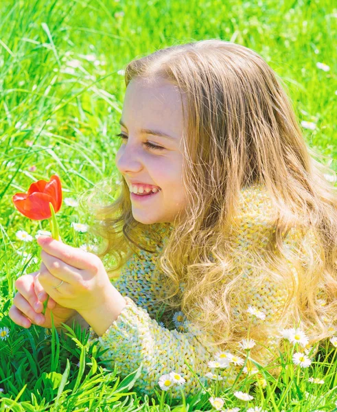 子供は、草原に横たわっている間チューリップの香りをお楽しみください。草地、草背景に横になっている長い髪を持つ少女。春の利益概念。幸せそうな顔の女の子は、晴れた春の日の赤いチューリップの花を保持しています。 — ストック写真