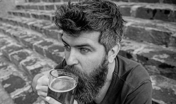 Hipster on excited face drinking beer outdoor. Friday relax concept. Man with beard and mustache holds glass with beer while sits on stone stairs. Guy having rest with cold draught beer — Stock Photo, Image