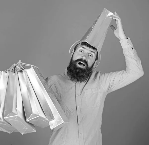 Férfi szakáll és bajusz hordozza bevásárló táskák, kék háttérrel. Vásárlás koncepció. Vásárlás az eladás szezont kedvezmények srác. Csípő a meglepett arcot zsákkal a feje rabja shopaholic — Stock Fotó