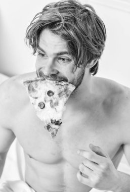 Adam yakışıklı bekar yatakta kahvaltı için peynirli yemek yeme sakallı. Yakışıklı adam bir parça pizza elinde tutar ve bu yemek. Hafta sonu.