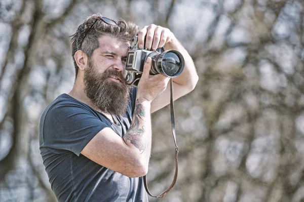 Skäggig man tar foto på solig dag. Fotograf koncept. Man med långt skägg upptagen med fotografering. Mannen med skägg och mustasch på koncentrerade ansikte, grenar på bakgrund, oskärpa — Stockfoto