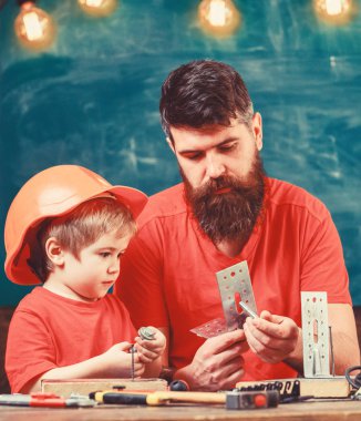 Evlat, Çocuk koruyucu kask içinde el ile onarım, babamla mı el sanatları yapar. Baba sakal ve araçlarını kullanmak için sınıf öğretim küçük oğlu kara tahta arka plan ile. Ana sayfa eğitim kavramı