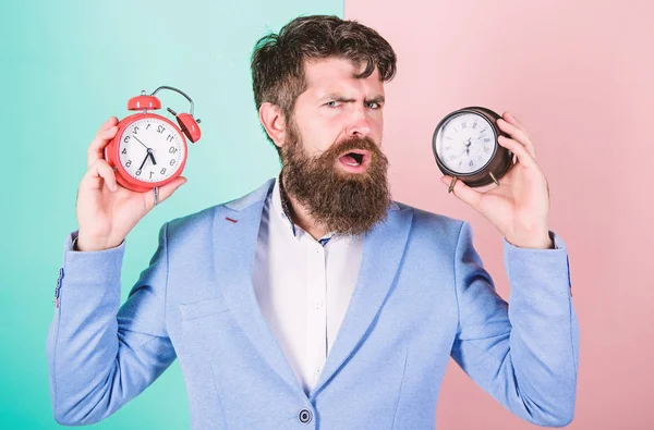 Guy unshaven puzzled face having problems with changing time. Time zone. Does changing clock mess with your health. Man bearded hipster hold two different clocks. Changing time zones affect health