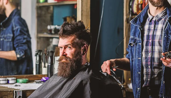 Barber with clipper and brutal bearded client. Hipster client getting haircut. Hipster lifestyle concept. Barber with hair clipper works on hairstyle for bearded man barbershop background