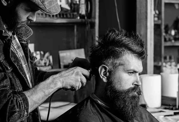 Un cliente hipster che si taglia i capelli. Barbiere con tagliacapelli lavora sull'acconciatura per uomo con barba, sfondo barbiere. Concetto di taglio. Il barbiere fa l'acconciatura usando clipper a uomo adulto con barba — Foto Stock