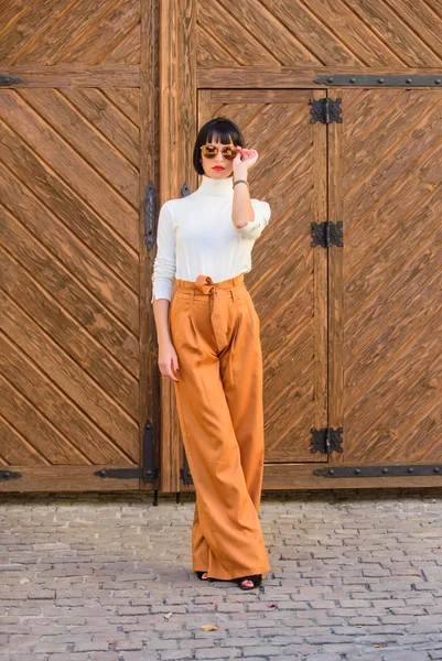 Fashion and style concept. Woman walk in loose pants. Woman fashionable brunette stand outdoors wooden background. Girl with makeup posing in fashionable clothes. Fashionable outfit slim tall lady — Stock Photo, Image