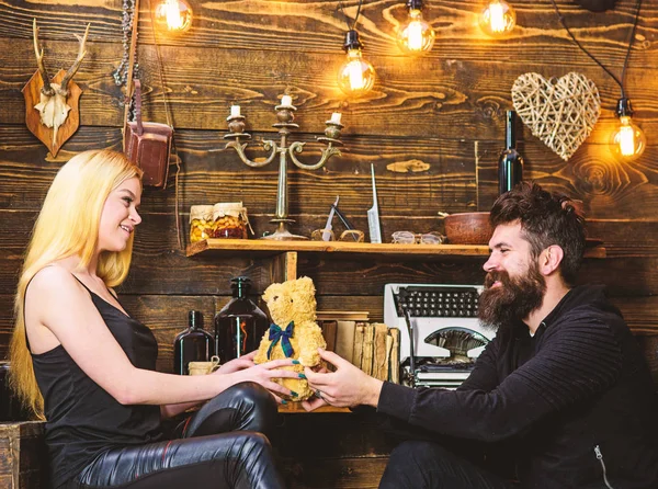 El hombre da a la señora osito de peluche como regalo en el aniversario. Concepto de aniversario. Pareja enamorada en caras sonrientes disfrutar de vacaciones. Pareja pasar una velada romántica en la casa de guardabosques, fondo interior de madera — Foto de Stock