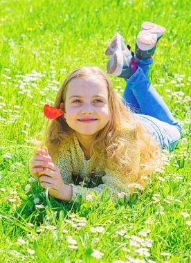 Uzun saç grassplot, çim arka plan yalan ile kız. Bahar ruh kavramı. Çocuk çayır yalancı bahar güneşli hava keyfini çıkarın. Yüz gülümseyerek kıza kırmızı lale çiçek tutan