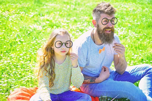 Zekice ve zekice bir fikir. Baba ve kızı yeşil arka planda çimlerin üzerinde oturuyorlar. Gözlüklerle poz veren çocuk ve baba çayırda fotoğraf kabini özellikleri. Aile dışarıda vakit geçirir.