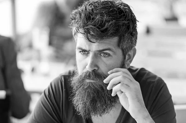 Mann mit Bart und Schnurrbart sitzt draußen auf Caféterrasse. Ein bärtiger Mann mit konzentriertem Gesicht streift den Schnurrbart. Hipster mit Bart wirken nachdenklich oder beunruhigt. Nachdenkliches Stimmungskonzept — Stockfoto