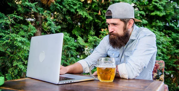 Using new technology. Bearded man communicating through communication technology. Hipster drinking beer and using laptop technology in outdoor cafe. Remaining productive with computer technology