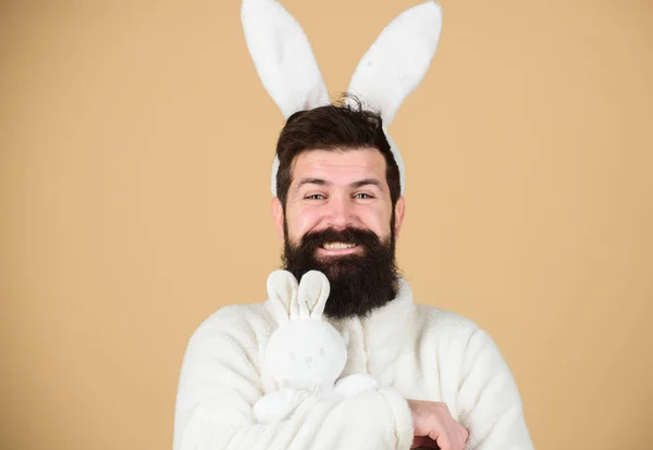 Bunny bringing gifts. Happy hipster with long rabbit ears holding bunny toy. Bearded man in easter rabbit costume with hare toy. Rabbit is a symbol of Easter and spring season. Fertility and new life