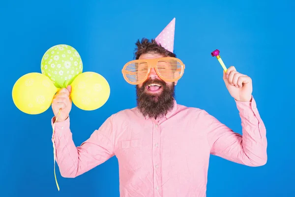 Man met baard en snor op blij gezicht houdt lucht ballonnen, blauwe achtergrond. Party concept. Hipster in gigantische brillen viert verjaardag. Guy in feest hoed met kenmerken die vakantie viert — Stockfoto