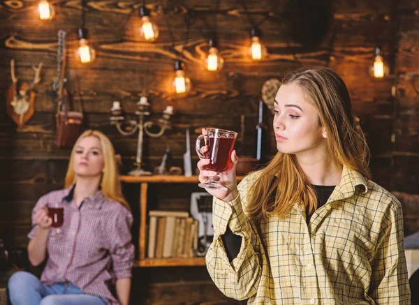 Friends on relaxed faces in plaid clothes relaxing, defocused. Friends enjoy mulled wine in warm atmosphere, wooden interior. Rest and relax concept. Girls relaxing and drinking mulled wine