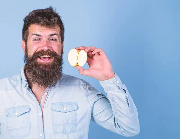 Hombre barbudo sonriente sostiene fondo azul manzana. La mitad del estilo de vida saludable manzana. Hipster demuestra manzana ecológica natural. Concepto de valor nutricional. Alimentación dietética para la salud vitamina nutrición — Foto de Stock