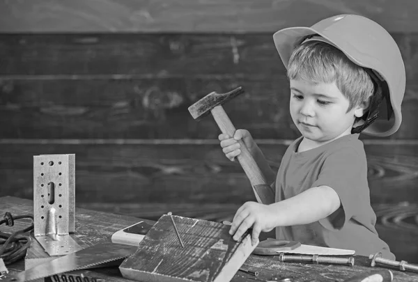 Kleinkind auf viel beschäftigtem Gesicht spielt zu Hause in der Werkstatt mit Hammerwerkzeug. Kind mit Helm spielt niedlich als Bauarbeiter oder Reparateur, repariert oder bastelt. Junge spielen als Handwerker. Bastelkonzept — Stockfoto