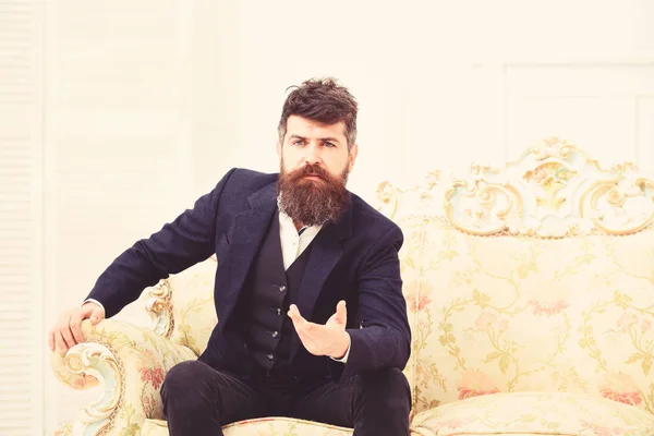 Homme avec barbe et moustache en costume classique, assis sur un fauteuil ou un canapé à l'ancienne. Conférencier, sage concept de conférencier. Macho attrayant et élégant sur le visage sérieux et expliquant l'expression — Photo