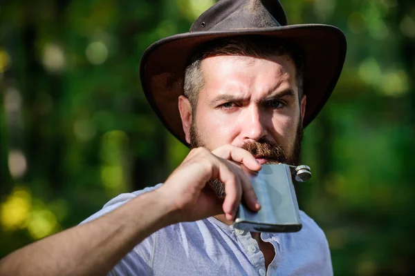 Wild West is his heart. camping and hiking. mature male with brutal look drink alcohol from flask. Bearded man in cowboy hat in park outdoor. man hipster relax in autumn forest. Spring sunny weather — Stock Photo, Image
