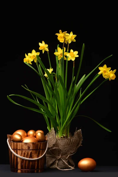 eggs in golden color inside bucket and bouquet of daffodils
