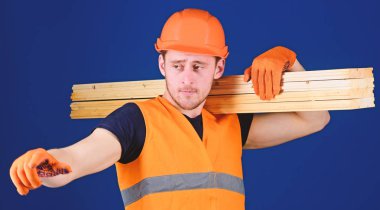 Ahşap malzemeler kavramı. Kask, kask ve koruyucu eldiven yön, mavi arka plan işaret eden adam. Marangoz, woodworker, meşgul yüz taşıdığı ahşap kiriş omuz üzerinde güçlü Oluşturucu