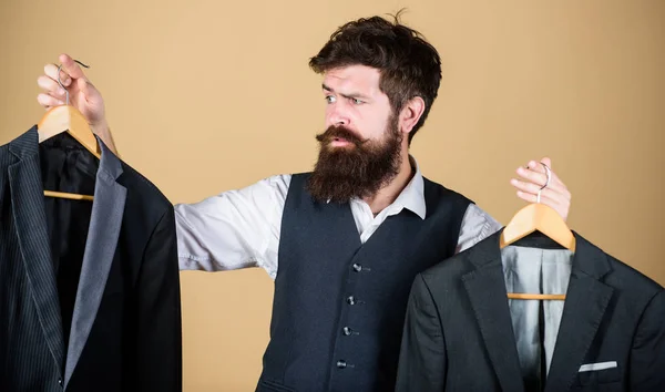 Facing hard choice. Hipster making shopping choice in shop. Businessman choosing which formal suit to wear. Choice of clothes. Bearded man holding suit jackets in store, choice concept