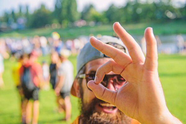 Мужчина бородатый на фоне толпы на берегу реки. Забронируйте билеты на летний фестиваль заранее. Фестиваль посещений хипстеров. Мужчина веселое лицо смотрит через хорошо жест. Будьте уверены в летнем отпуске
