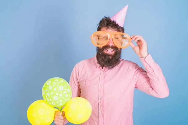 Glad skäggig man i enorma glasögon poserar med ljusa ballonger, kul koncept. Komiker med galen ser underhållande gäster vid särskilda evenemang. Lokalvårdare med vilda skägg vägledande tävling på födelsedagsfest — Stockfoto