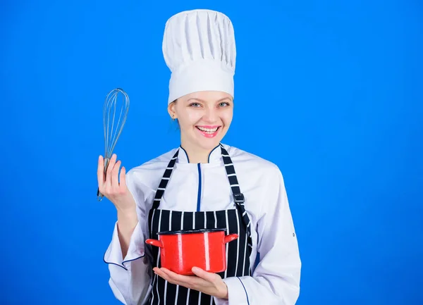 Handling kitchen tasks with ease. Professional cook smiling with pot and whipping tool in kitchen. Cute kitchen maid with whisk and mixing bowl. Happy cook holding kitchen tool and utensil