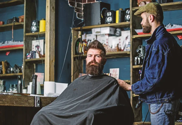 Hipster client got new haircut. Barber with hair clipper looking at mirror, barbershop background. Haircut concept. Professional master checking result while client sits in chair. Barber done haircut