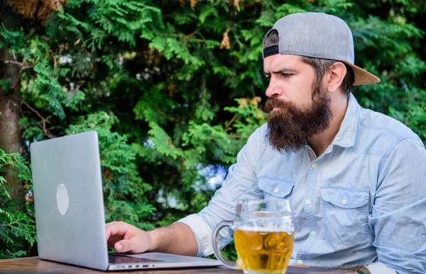 Finally friday. Hipster relax sit terrace with beer. Bearded hipster freelancer enjoy end of working day with beer mug. Beer helps him relax after hard day. Brutal man leisure with beer and laptop