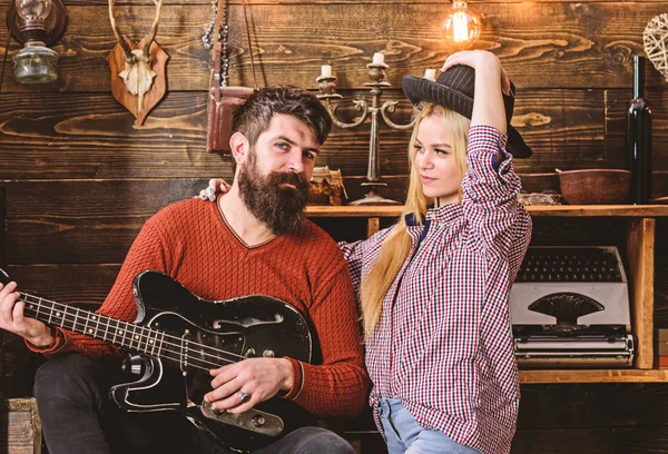 Romantic evening concept. Lady and man with beard on happy faces hugs and plays guitar. Couple in love spend romantic evening in warm atmosphere. Couple in wooden vintage interior enjoy guitar music