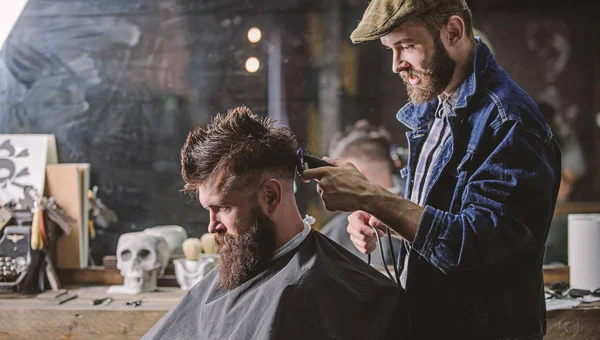 Barber with clipper trimming hair on nape of client. Barber with hair clipper works on haircut of bearded guy barbershop background. Hipster hairstyle concept. Hipster client getting haircut