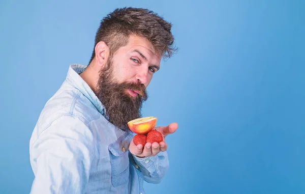 Ich habe Leckereien für dich. Hipster-Bärtiger hält Erdbeeren und Apfel auf Palmen. Schlaues Gesicht mit Bart bietet Bio-Leckereien. Mann bietet Erdbeeren und Apfelfrucht Leckereien blauen Hintergrund versuchen — Stockfoto