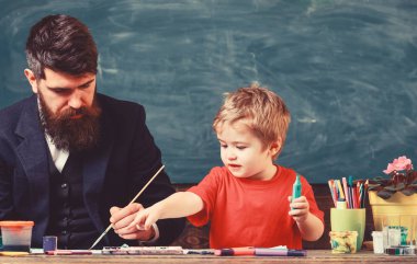 Sakallı öğretmeni, sınıfta, kara tahta arka plan çizmek için küçük oğlu baba öğretir. Sanat ders kavramı. Yetenekli sanatçı oğlu ile vakit geçirmek. Çocuk ve resim öğretmeni meşgul yüz boyama,
