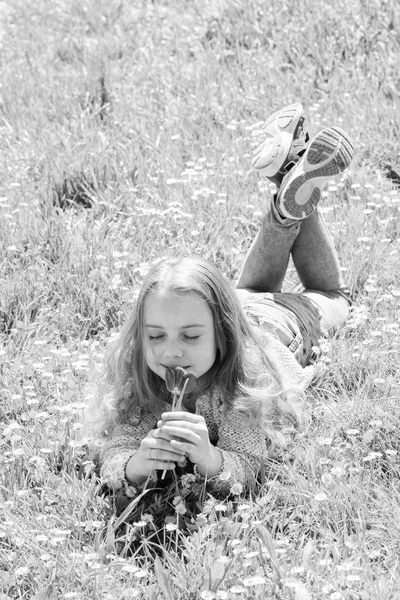 Dziewczyna z długimi włosami leżącego na trawnik, trawa tło. Dziecko cieszyć zapach tulipanów, leżąc na łące. Dziewczyna na spokojną twarz trzyma kwiat czerwony tulipan w słoneczny wiosenny dzień. Koncepcja mood wiosna — Zdjęcie stockowe