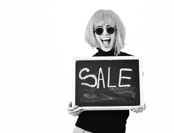 Fashionable girl in wig holding board with sale inscription — Stock Photo, Image