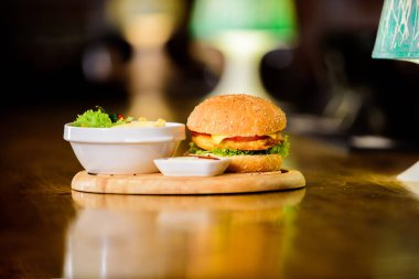 Fast-Food konsepti. Peynirli et ve salata ile Burger. Hile yemek. Susam ile lezzetli burger. Burger menüsü. Yüksek kalorili atıştırmalıklar. Ahşap tahta üzerinde hamburger ve patates kızartması ve domates sosu