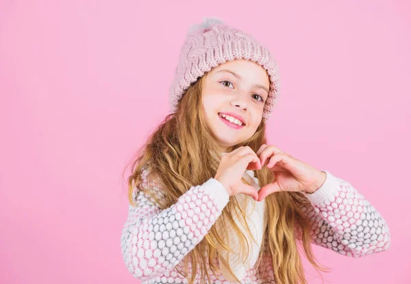 Look after scalp and hair this winter. Prevent winter hair damage. Winter hair care tips you should follow. Child long hair smiling show heart gesture. Girl wear knitted hat pink background