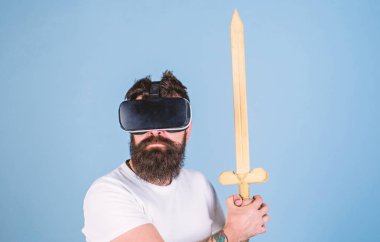 Oyun kavramı. Hipster ciddi bir yüz üzerinde sanal gerçeklik oyun oyun keyfini çıkarın. Vr gözlük, açık mavi renkli sakallı adam. Adam kafa monte ekran ile kılıç, oyun Vr oyunda mücadele tutar