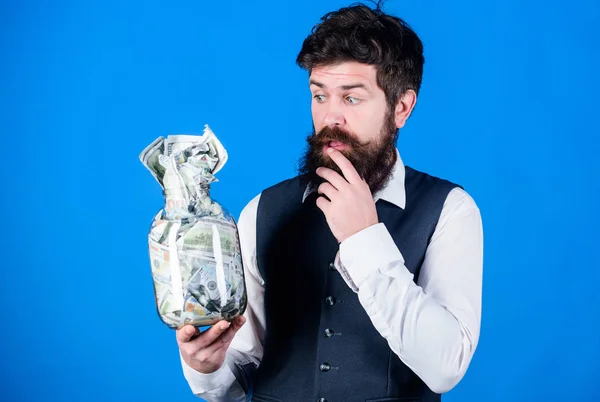 Takes money to make money in his business. Bearded man think of investing money in startup business. Businessman holding money in glass jar. Business and finance. Business savings