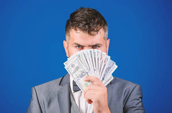 Get cash money easy and quickly. Smell of money. Easy cash loans. Man formal suit hold pile of dollar banknotes blue background. Businessman got cash money. Richness and wellbeing concept