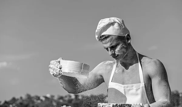 Muž svalnaté baker nebo kuchař sifts přes síto mouku. Rukou šéfkuchař Cook pokryté lepivé těsto a mouku. Baker na práci s moukou a síta, hnětení těsta. Koncept dělat koktejl — Stock fotografie