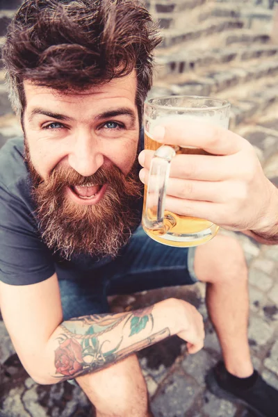 Ο άνθρωπος με το γυαλί κατέχει γένια και μουστάκι με μπύρα, ενώ κάθεται σε πέτρινα σκαλοπάτια. Hipster στο χαρούμενο πρόσωπό πίνοντας μπύρα εξωτερική. Ο τύπος με τατουάζ έχοντας υπόλοιπο με κρύα μπύρα. Παρασκευή χαλαρώσετε έννοια — Φωτογραφία Αρχείου