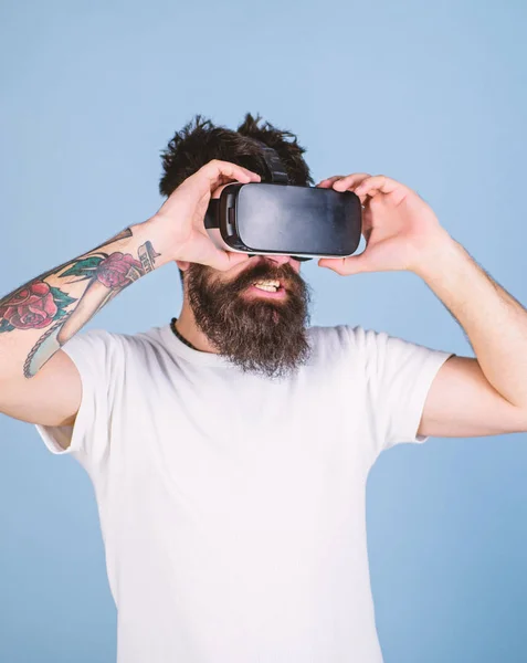 Man with long beard having cyber experience in VR glasses, digital innovations concept. Bearded man testing new device. Hipster with tattooed arm and stylish beard amused by 3D virtual reality video