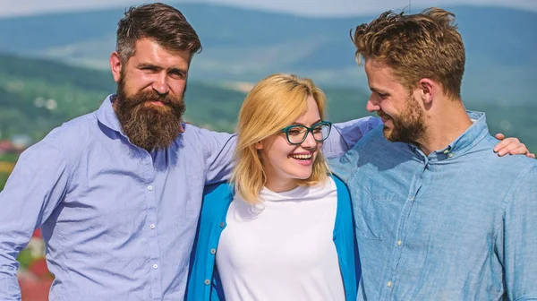 Company of three happy colleagues or partners hugs outdoor, nature background. Men with beard in formal shirts and blonde in eyeglasses as successful team. Business team concept. Company reached top